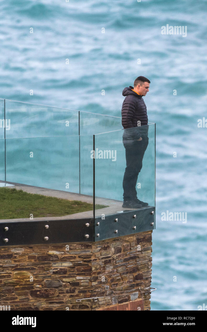 Un uomo in piedi da solo su un balcone che guarda al mare. Foto Stock