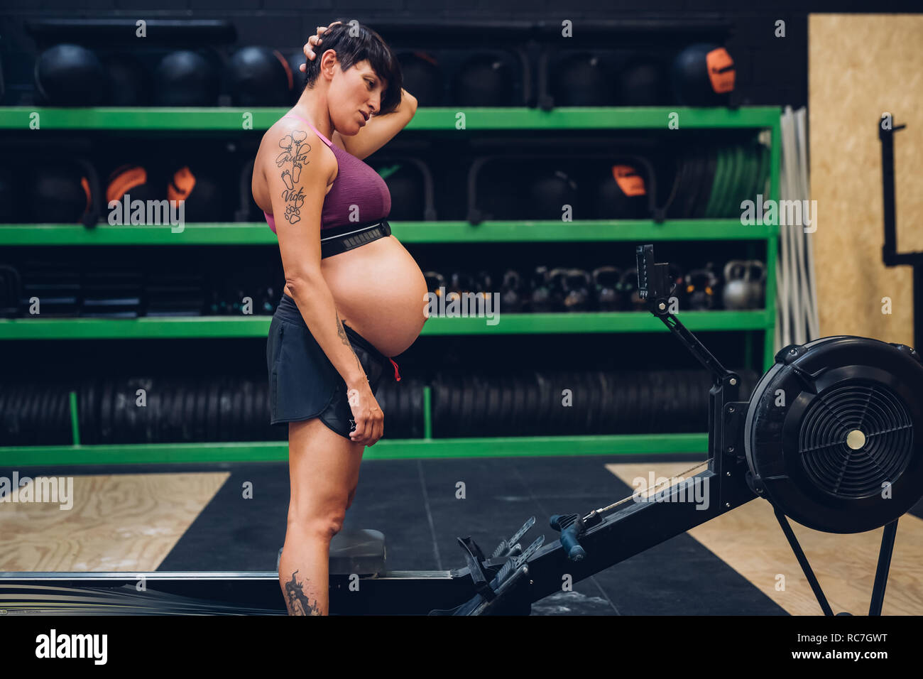 Donna incinta guardando vogatore in palestra Foto Stock