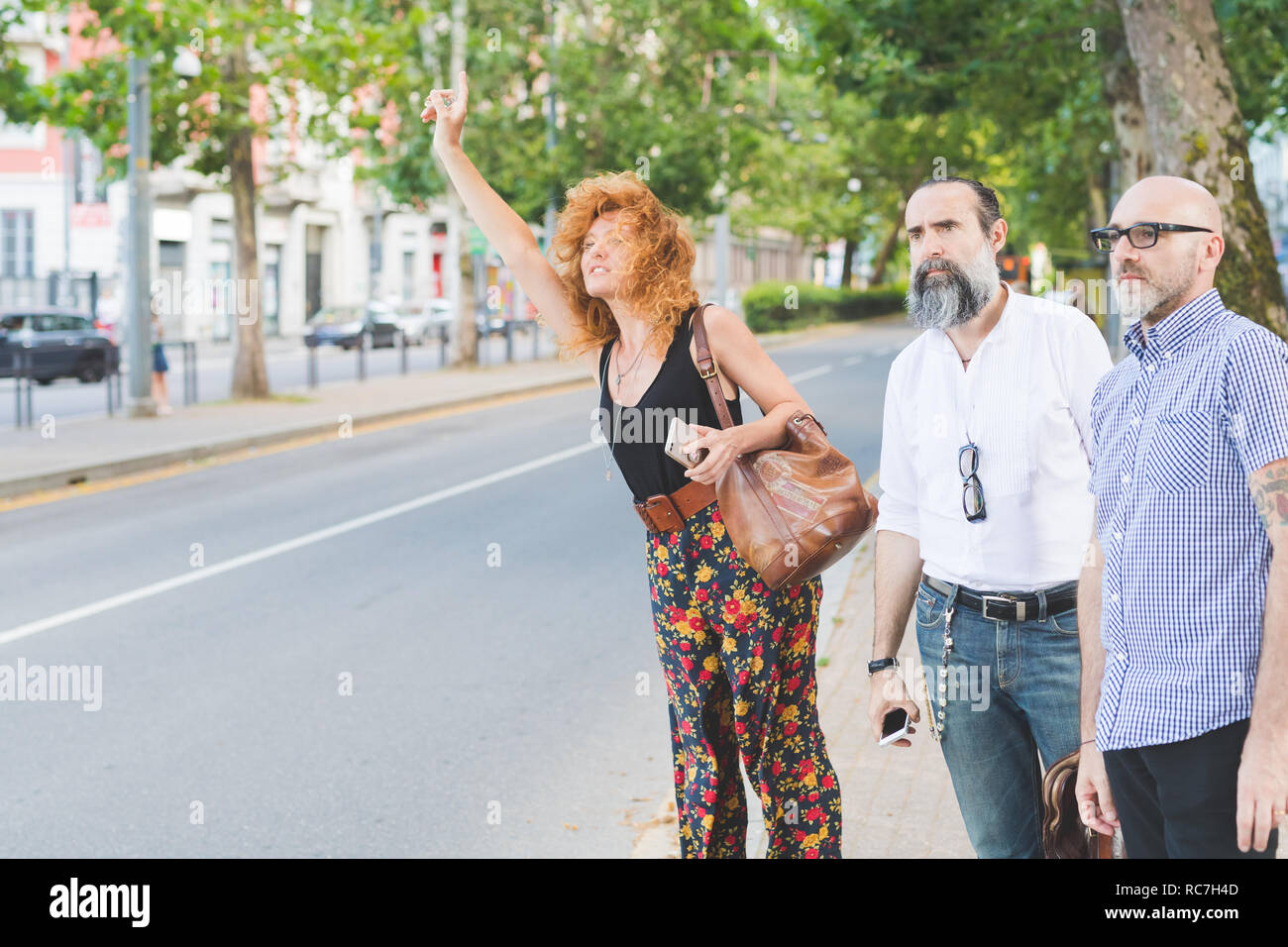 Metà donna adulta e amici maschi salutando un taxi sulla strada di città Foto Stock