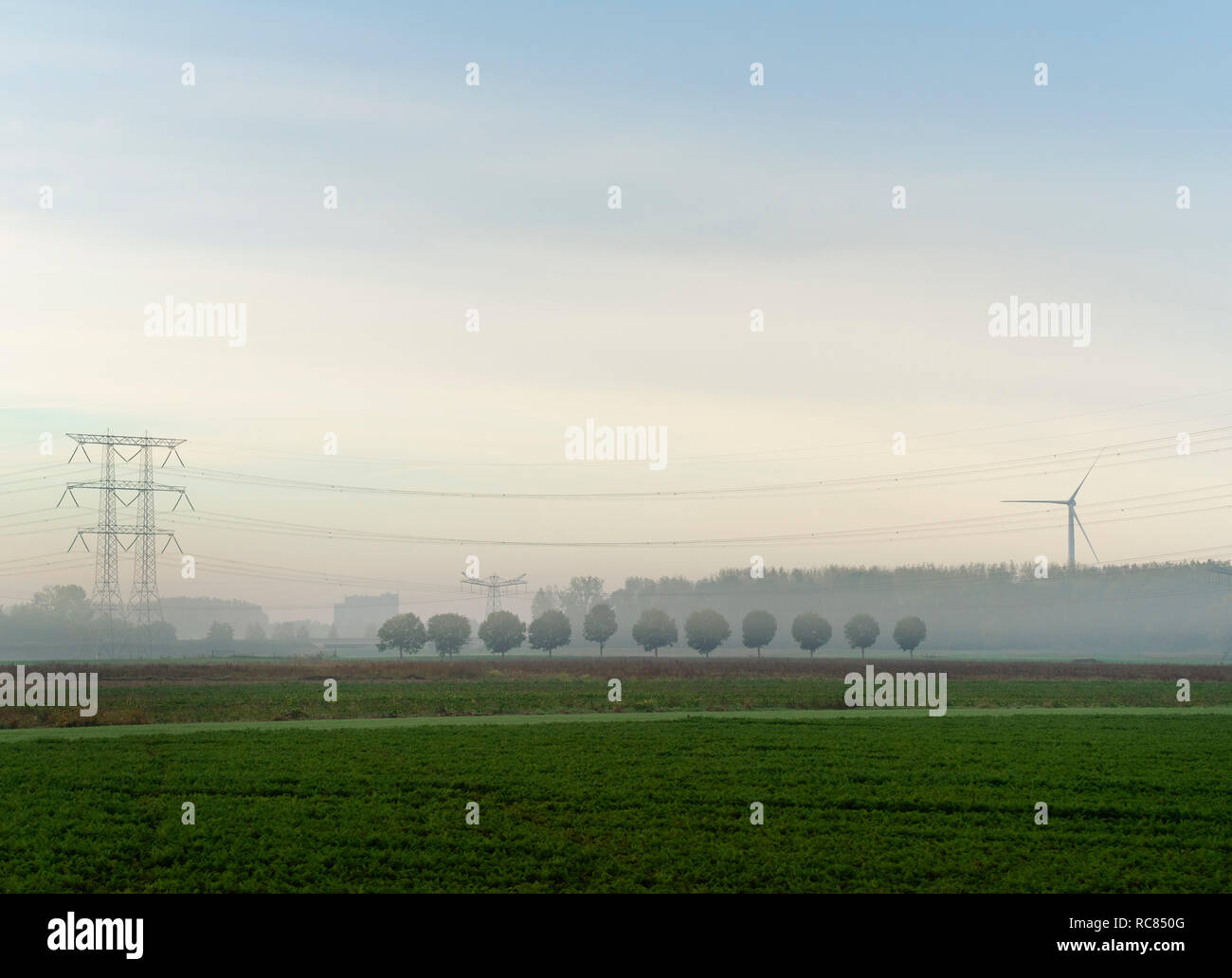Paesaggio con turbina a vento e linee di alimentazione su una mattinata nebbiosa, Paesi Bassi Foto Stock
