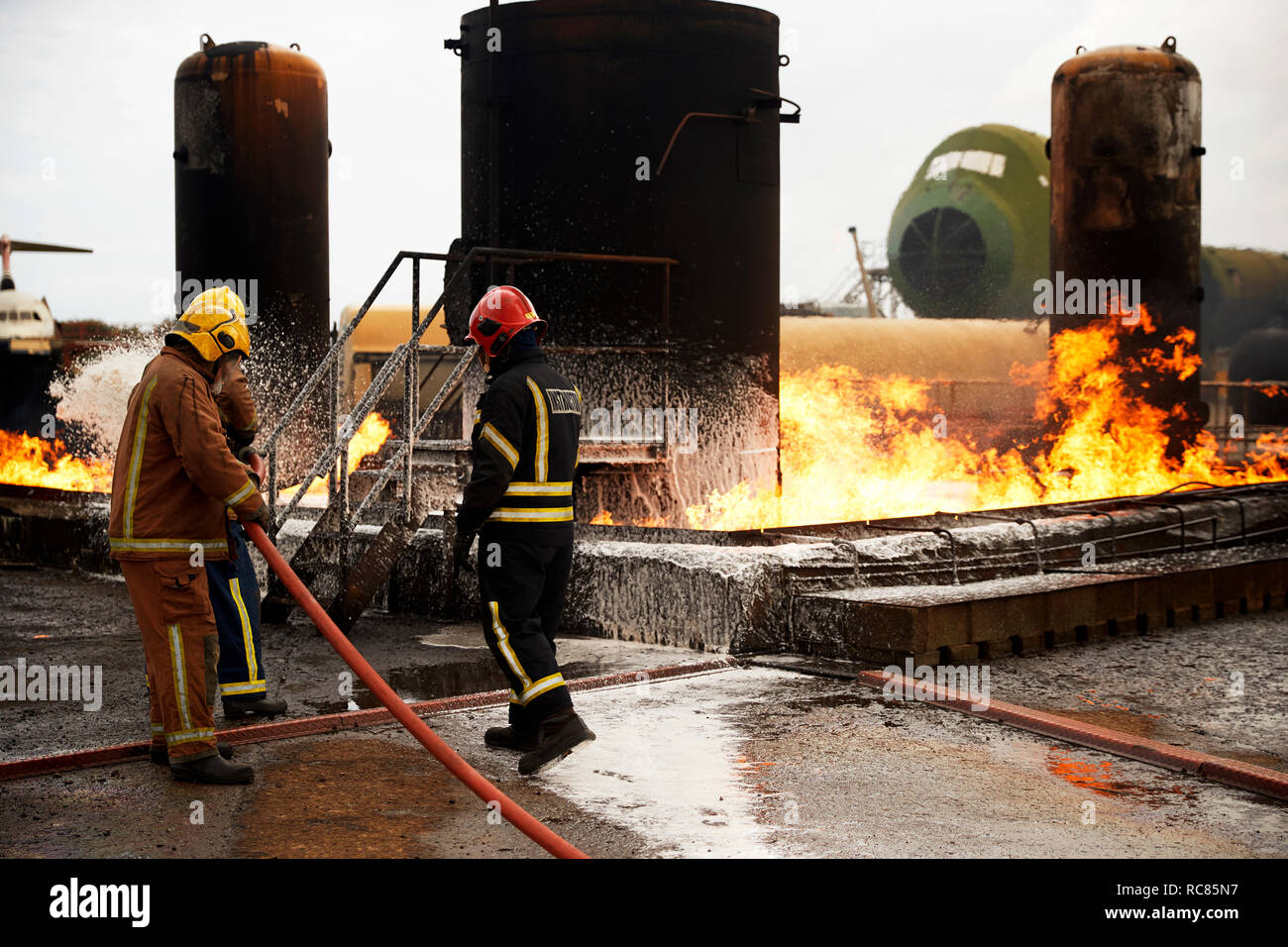 Addestramento vigili del fuoco, la spruzzatura di schiuma antincendio sul serbatoio di accumulo di olio a fuoco training facility Foto Stock
