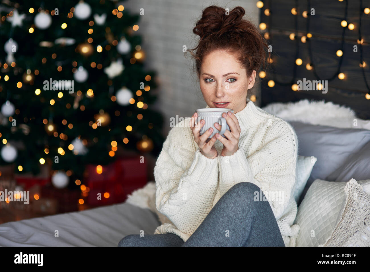 Donna con bevanda calda sul letto decorato con luci di Natale Foto Stock