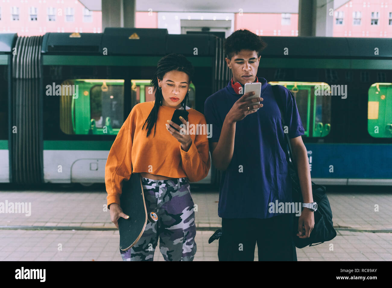 Fratello e Sorella texting alla fermata del tram, Milano, Italia Foto Stock