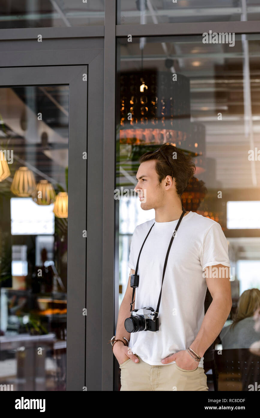 Fotografo con fotocamera attorno al collo in attesa per cafe ingresso Foto Stock