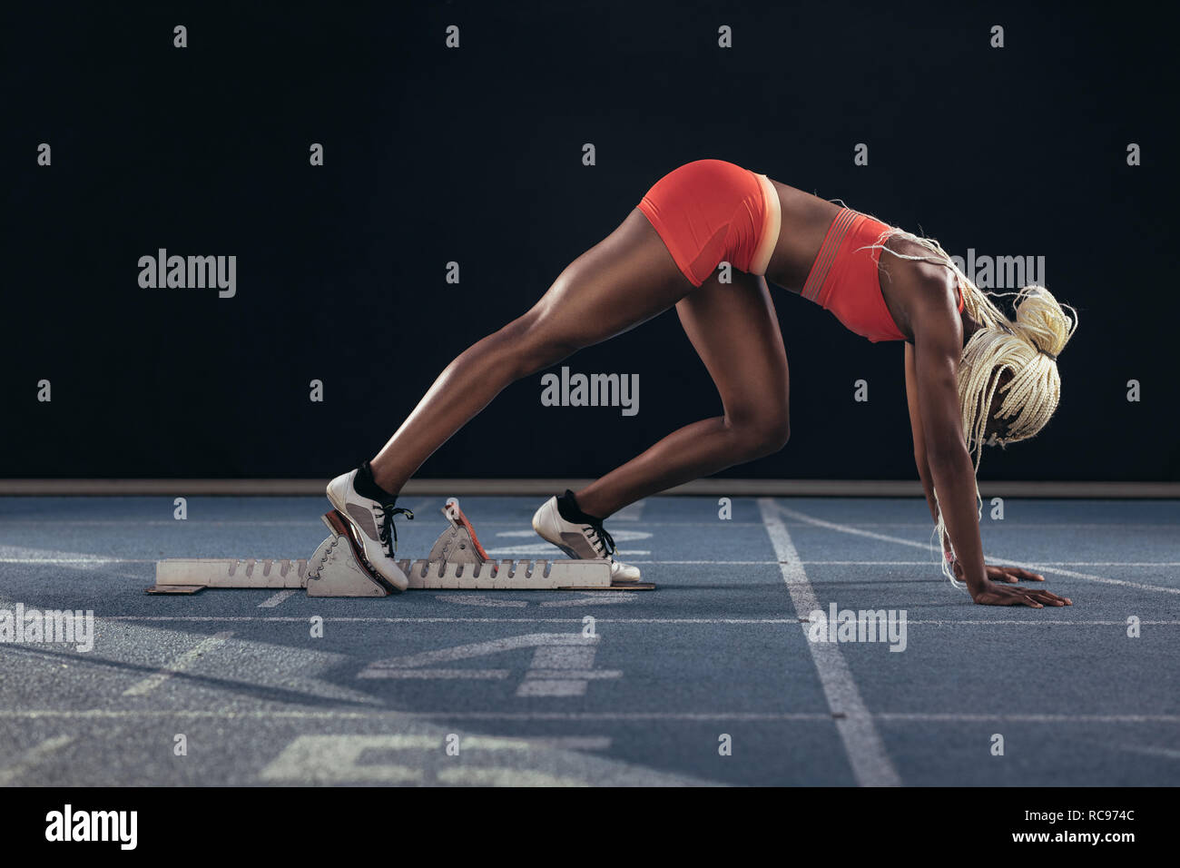 Atleta femminile di prendere posizione sul suo segna per iniziare la corsa. Vista laterale del femminile ottenere pronto per la gara in linea di partenza sulla via di corsa Foto Stock