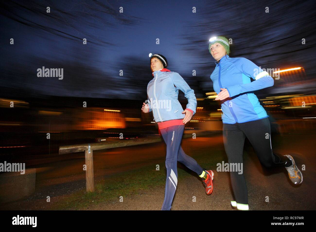 Due giovani donne jogging al tramonto in abbigliamento invernale con strisce riflettenti, fari a LED e dal vento funzionale impermeabile Foto Stock