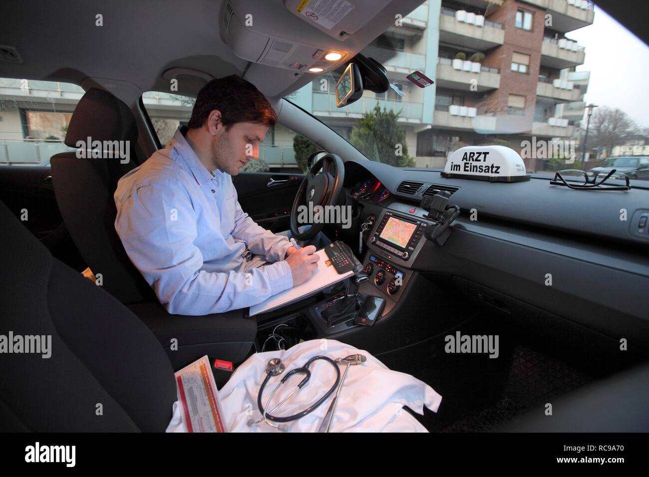Giovani GP, medico di medicina generale prendendo appunti nella sua auto dopo una visita a casa, auto visualizzando il segno "Arzt im Einsatz" Foto Stock