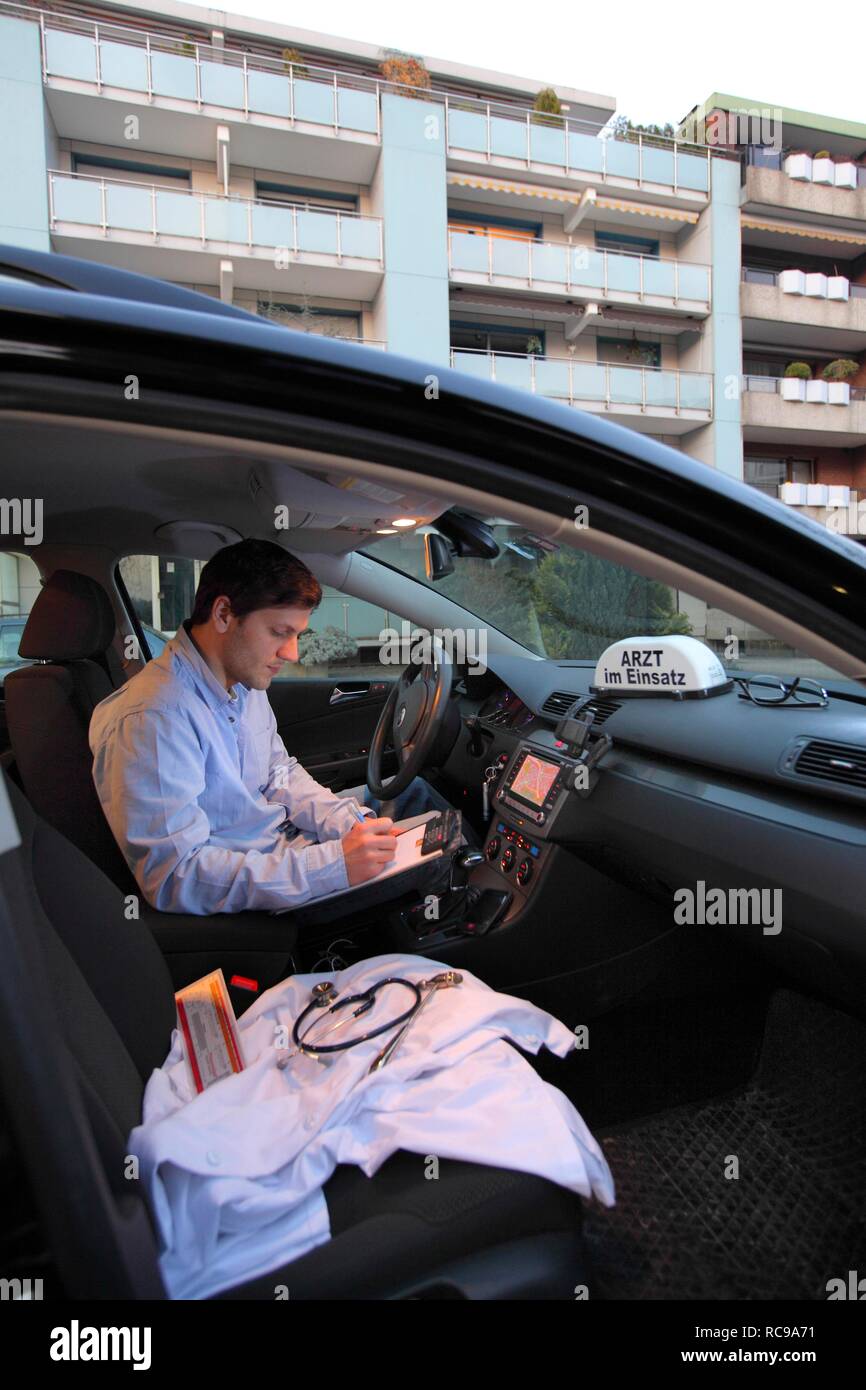 Giovani GP, medico di medicina generale prendendo appunti nella sua auto dopo una visita a casa, auto visualizzando il segno "Arzt im Einsatz" Foto Stock