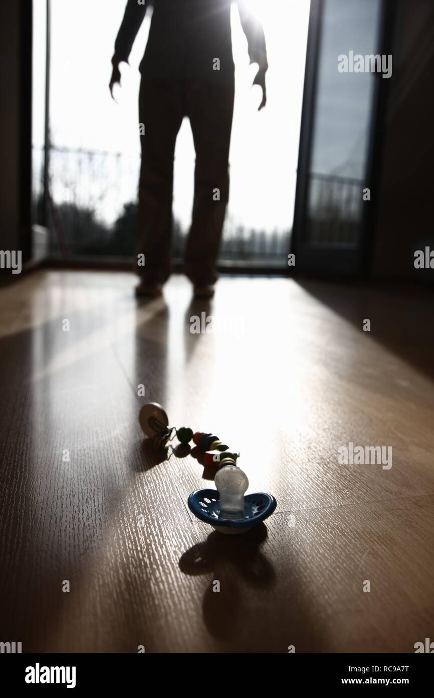 Succhietto sdraiato sul pavimento di fronte a una silhouette di una persona, immagine simbolica per gli abusi sui minori, la violenza contro i bambini Foto Stock