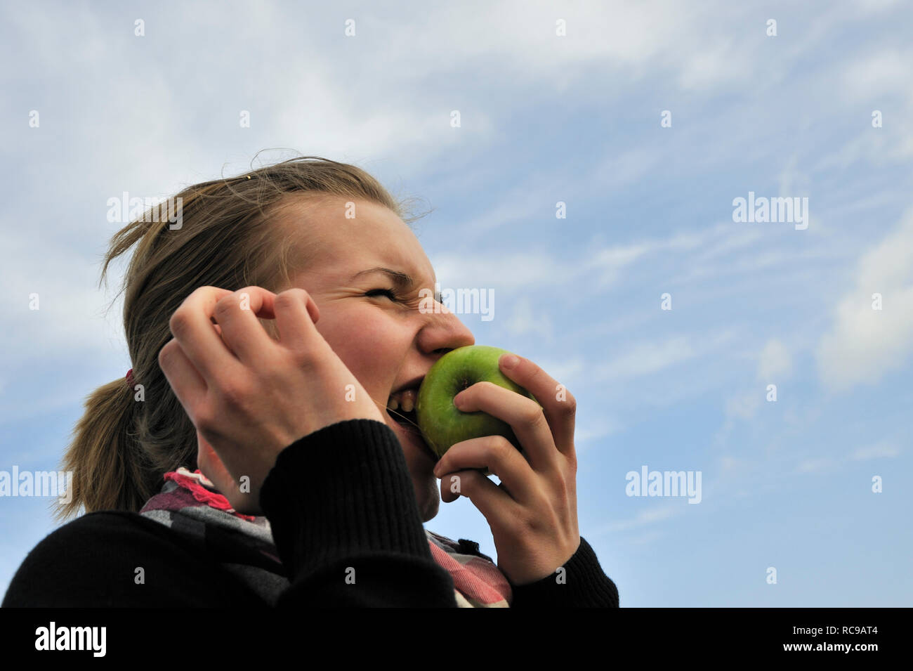 Junge Frau beisst in einen grünen Apfel - in den sauren Apfel beissen | giovane donna mangia una mela verde - per ingoiare una pillola amara o per afferrare il natt Foto Stock