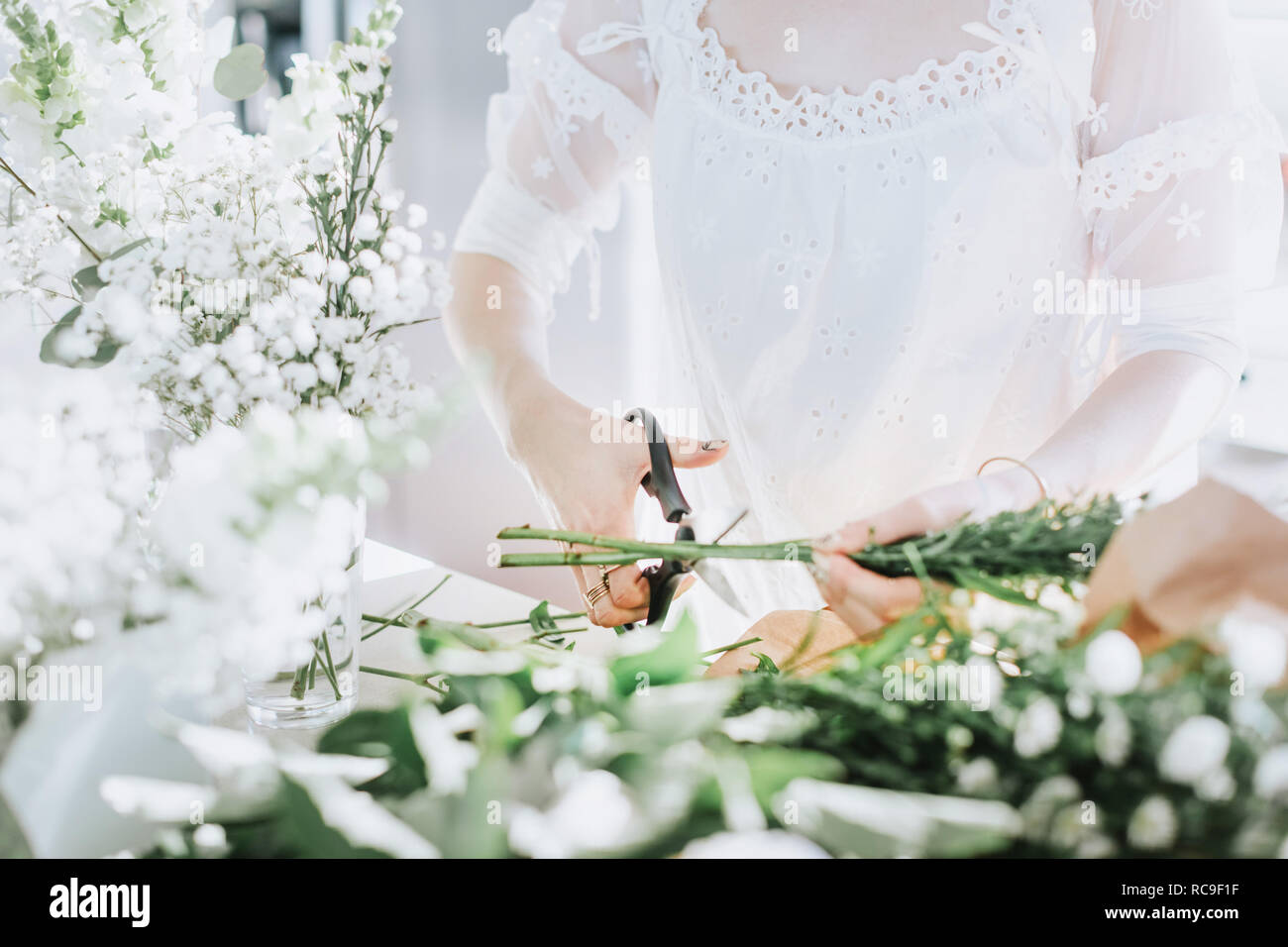 Giovane donna in abito bianco il taglio di fiori bianchi, metà sezione Foto Stock