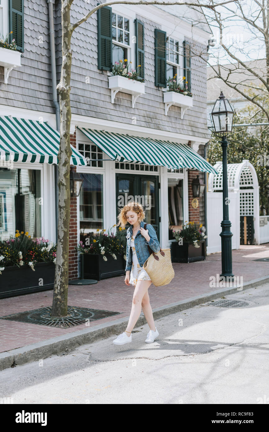 Giovane donna passeggiando lungo la strada che porta sacchetto di paglia, Menemsha, Martha's Vineyard, Massachusetts, STATI UNITI D'AMERICA Foto Stock