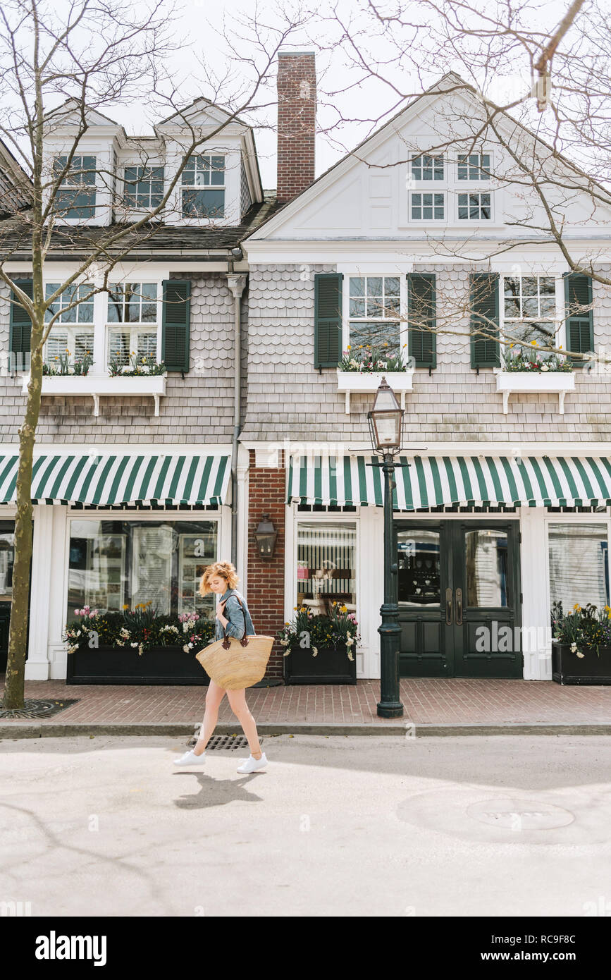 Giovane donna passeggiando lungo la strada che porta sacchetto di paglia, Menemsha, Martha's Vineyard, Massachusetts, STATI UNITI D'AMERICA Foto Stock