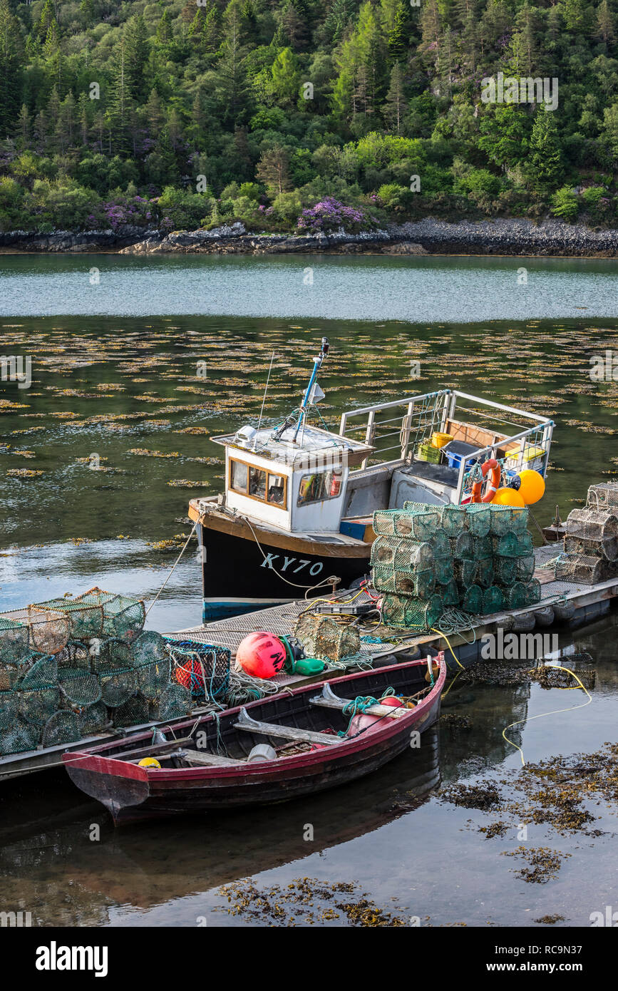 Ormeggiate piccole barche da pesca e pentole di aragosta / boreale cantre impilati sul molo nel Plockton Harbour, Highlands scozzesi, Scotland, Regno Unito Foto Stock