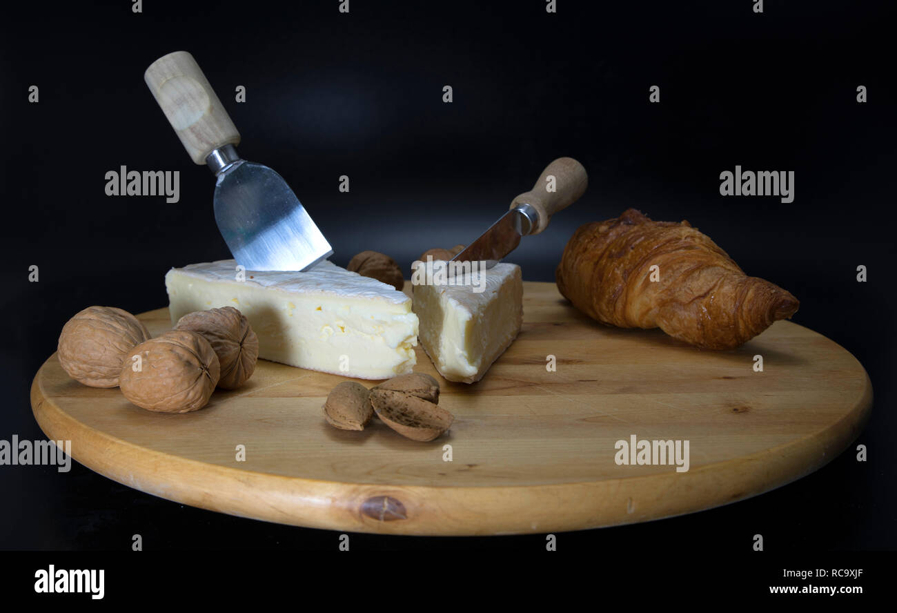 In legno piatto girevole con formaggio francese chiamato brie con la lama di un coltello e un croissant francesi e le noci e mandorle Foto Stock