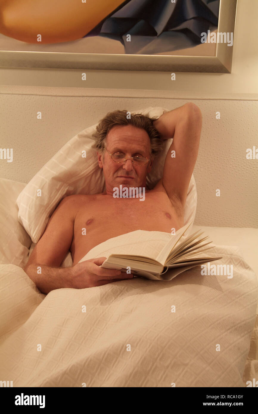 Mann mittleren altera liest ein Buch im Bett | middleaged l uomo è la lettura di un libro a letto Foto Stock