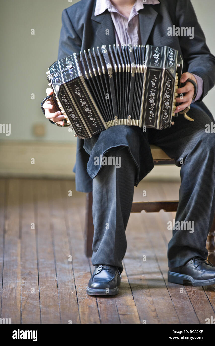 Le gambe di un giovane adulto uomo seduto di suonare la fisarmonica in una stanza. Foto Stock