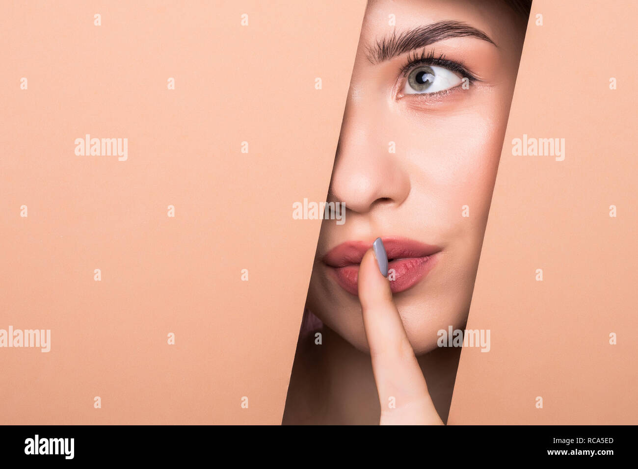 Il volto del giovane bella ragazza con un luminoso make-up e puffy orange labbra coetanei in un foro nella carta di pesche. Foto Stock