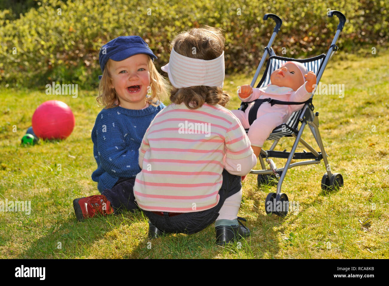 Zwei kleine Mädchen, 2 Jahre alt, spielen mit einer Puppe Puppenbuggy im | due bambine di due anni, a giocare con la loro bambola Foto Stock