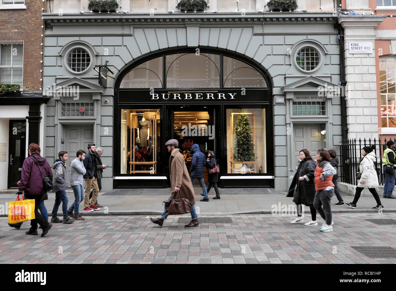 Persone acquirenti e uomo portare borsa a piedi oltre Burberry negozio esterno a Natale a Covent Garden Londra Inghilterra Regno Unito KATHY DEWITT Foto Stock