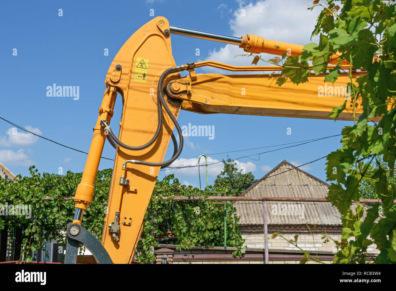 Close-up i dettagli di costruzione stradale macchina dipinta di giallo sul blu del cielo e il verde delle foglie di piante di uva sfondo in condizioni di luce solare intensa sul sobborgo street. Foto Stock
