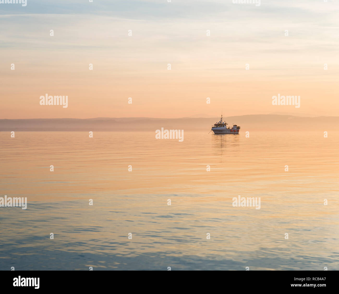 Tranquillo e pacifico tramonto a Isola Santa producendo alcuni graziosi caldi colori pastello nel cielo e mare e scontornamento la barca da pesca & paesaggio splendidamente. Foto Stock