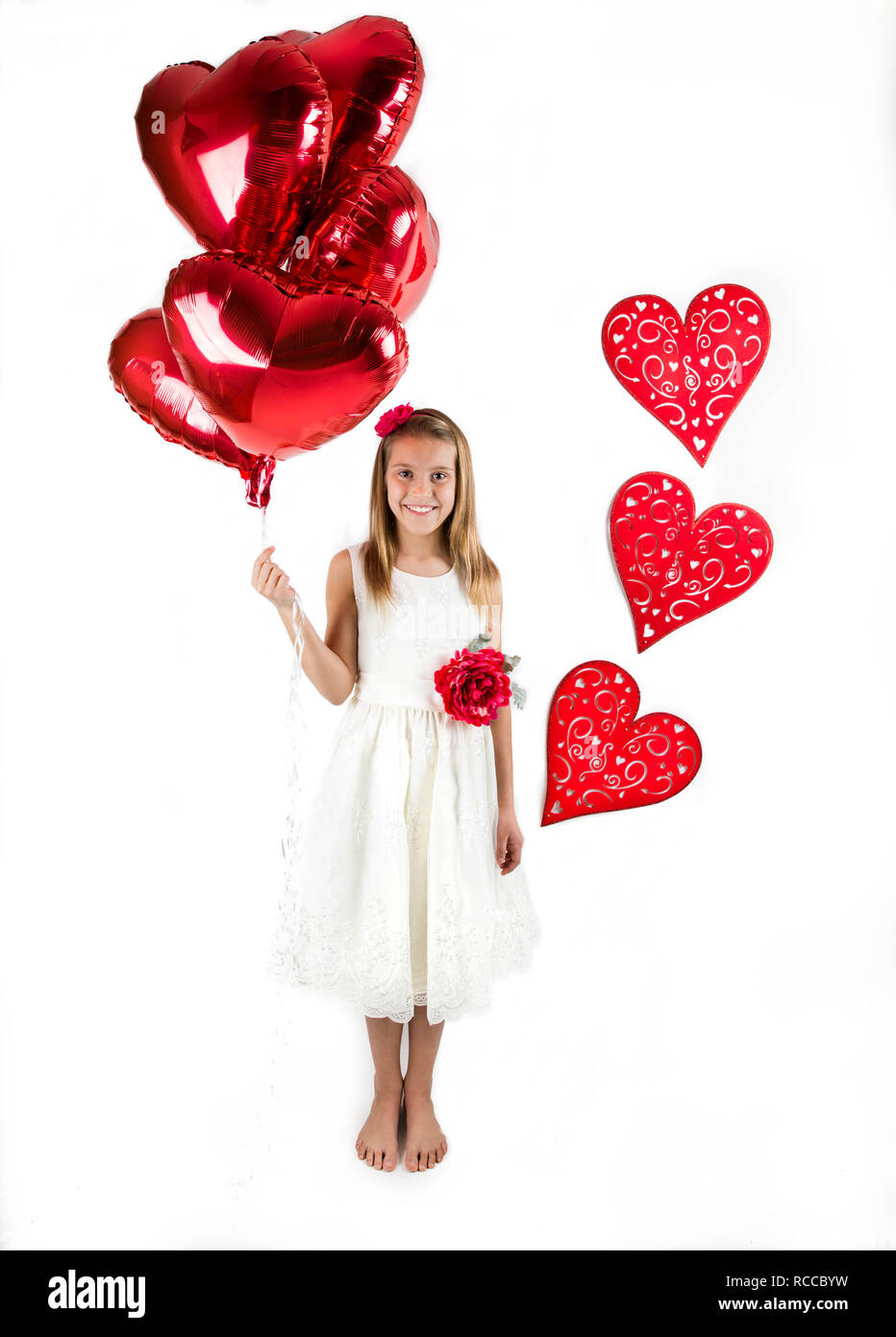 Graziosa bambina con abito bianco per celebrare il giorno di San Valentino e azienda lucido rosso palloncini a forma di cuore su sfondo bianco Foto Stock