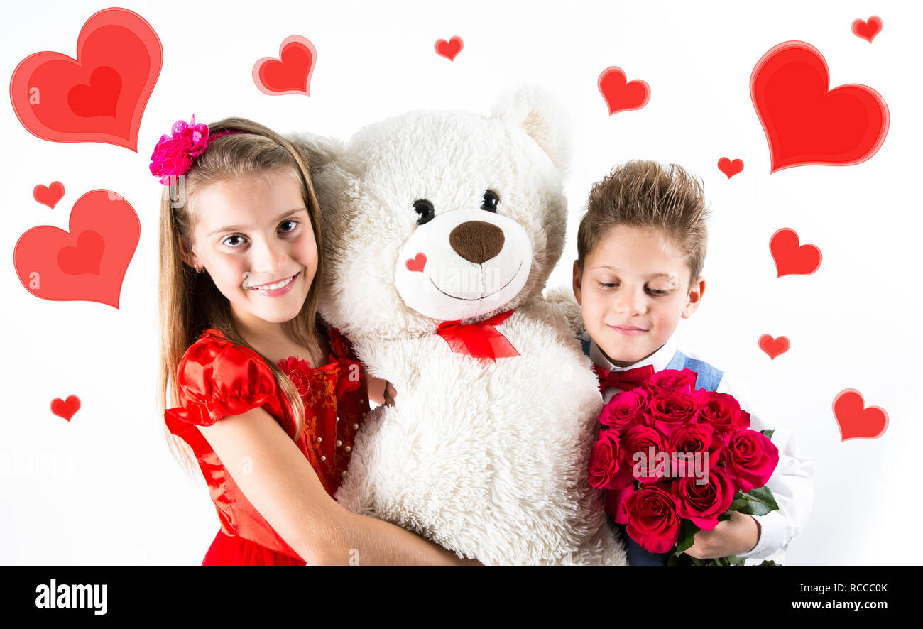 Grazioso e piccolo ragazzo e una ragazza che celebra il giorno di San Valentino e azienda rose rosse benna e orso bianco dono sullo sfondo bianco con cuore rosso Foto Stock