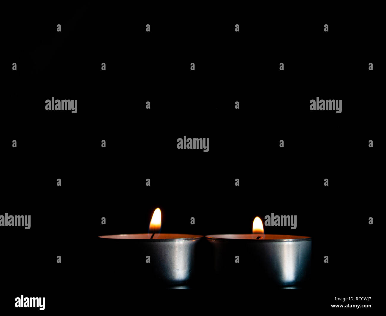 Due candele accese con una fiamma di colore arancione e isolate su uno sfondo nero Foto Stock