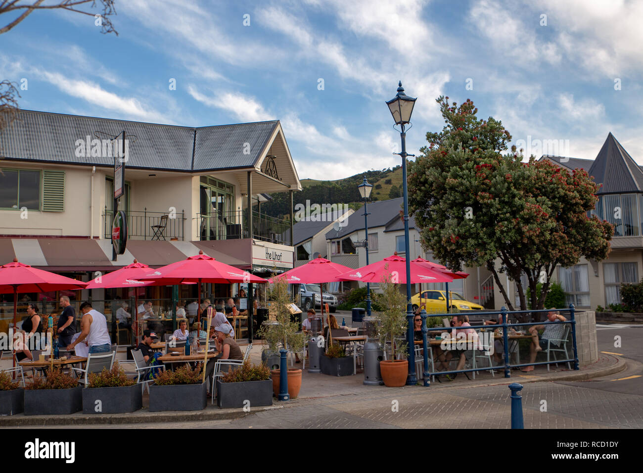 Akaroa, Penisola di Banks, Nuova Zelanda - Gennaio5 2019: turisti cenare fuori sotto gli ombrelloni presso Il Wharf Restaurant in una calda serata estiva Foto Stock