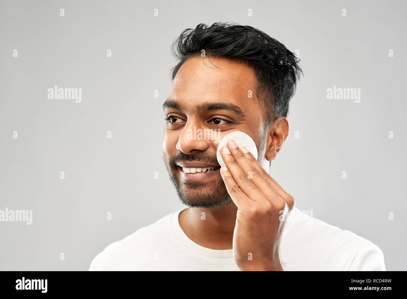 Sorridente uomo indiano la pulizia viso con tampone di cotone Foto Stock