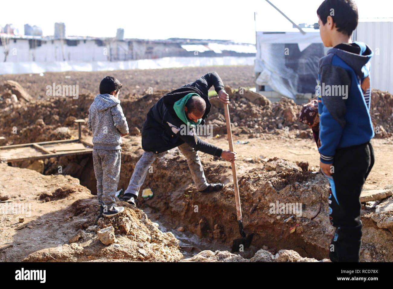 Un rifugiato siriano scava un canale per deviare l'acqua di allagamento da un fiume vicino lontano da tende. Tempesta Norma colpite migliaia di profughi siriani che vivono in condizioni precarie in Libano Bekaa valley. Ora sono costretti di essere preparato per un altro dalla tempesta che si avvicina. Foto Stock