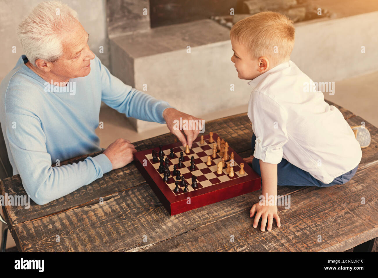 Gioco per gli intellettuali. La vista in pianta di un piacevole amorevole nonno e la sua amata nipote seduta al tavolo e giocare a scacchi insieme sul Foto Stock