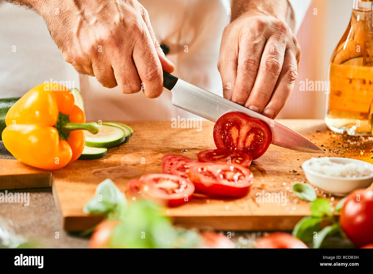 Lo Chef un taglio fresche e mature di pomodoro rosso con un grande elemento tagliente coltello da cucina in una stretta fino alle mani Foto Stock