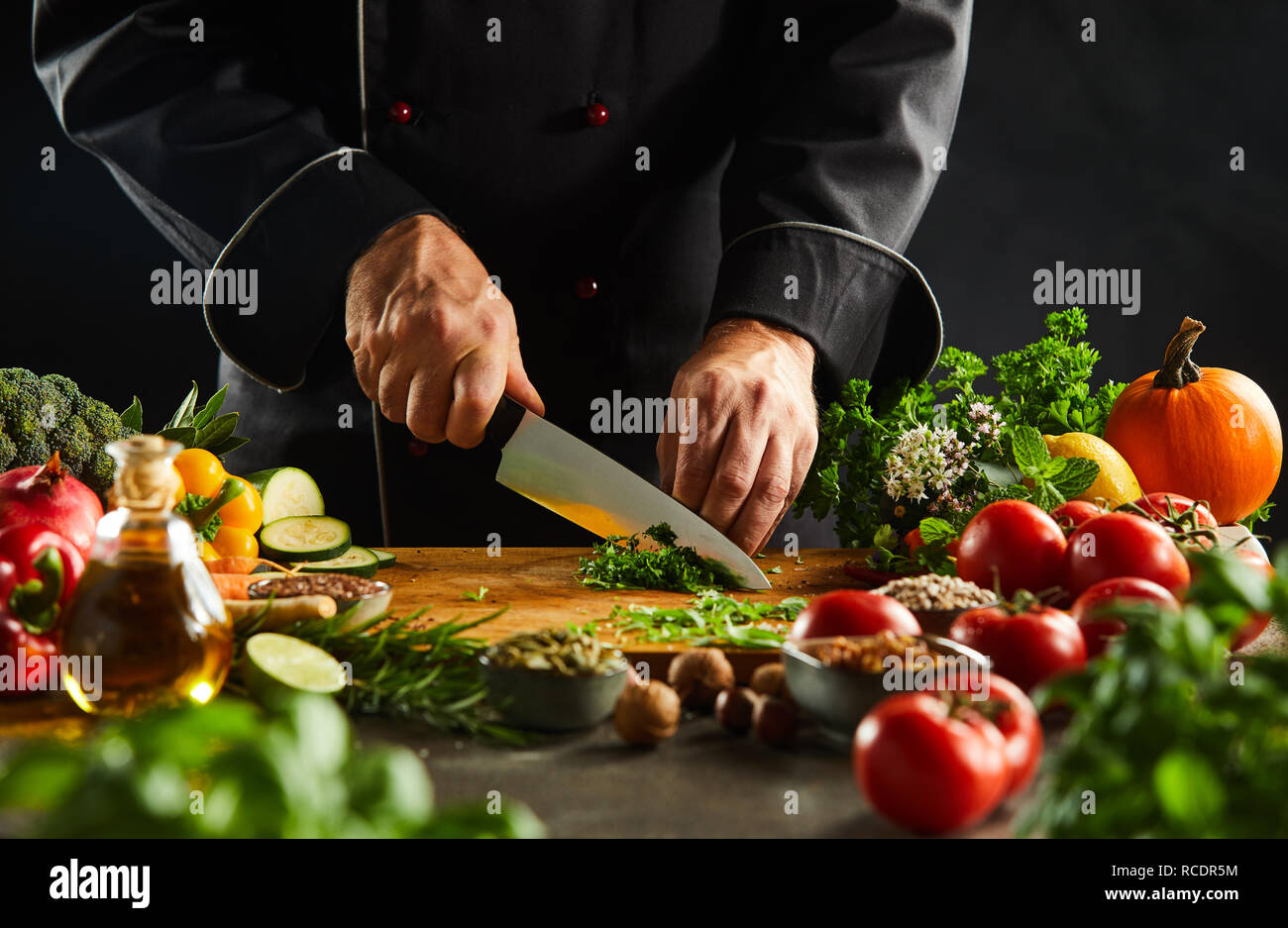 Lo Chef cubettatura erbe fresche su un tagliere di legno con un coltello da cucina durante la preparazione di insalata in una stretta fino alle mani Foto Stock