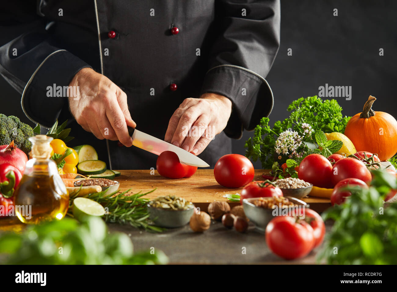 Chef per affettare ingredienti insalata in un ristorante il taglio di un maturo di pomodoro rosso con un coltello affilato su una tavola di legno in una stretta fino alle mani Foto Stock