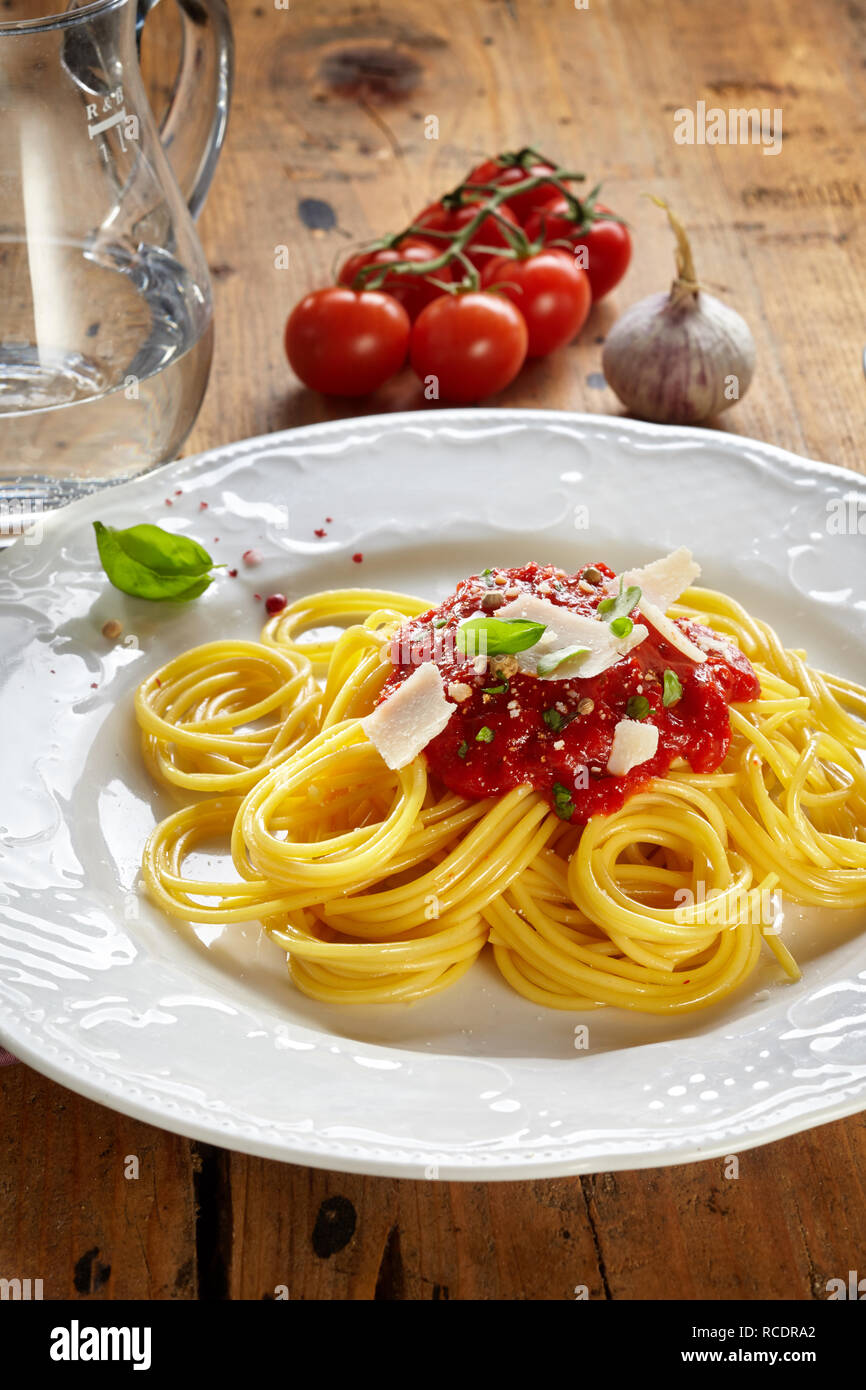 Italian spaghetti bolognese con egg noodles guarnita con un fresco condito salsa di pomodoro guarnita con formaggio Parmigiano servito su una piastra bianca con ve Foto Stock