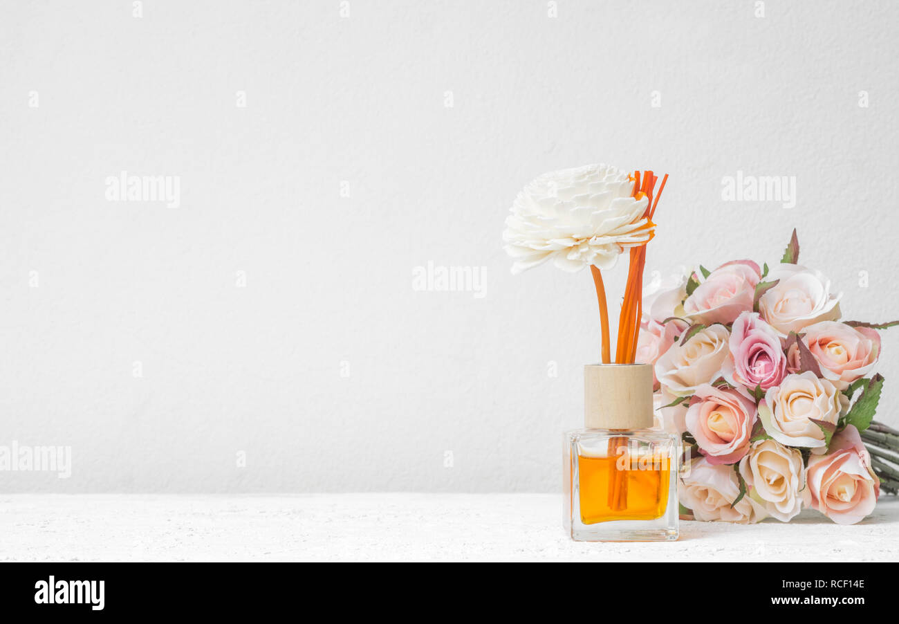 Reed aromatico rinfrescante, diffusore di fragranze Set di bottiglia con bastoni di aroma (reed diffusori) con rose fiore sul muro bianco sullo sfondo. Foto Stock