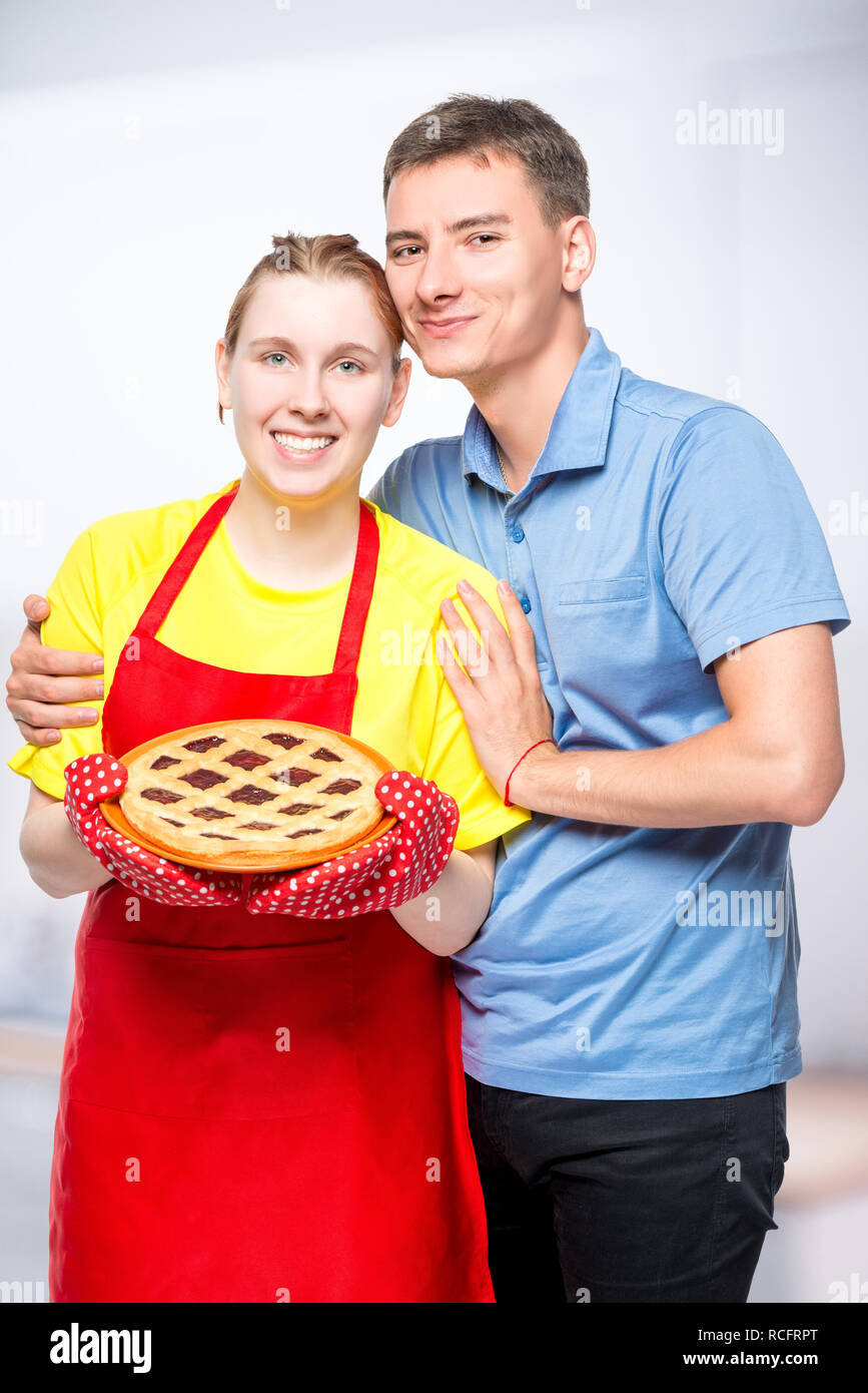 Casalinga in grembiule con una torta e il suo amato sposo, ritratto in cucina Foto Stock