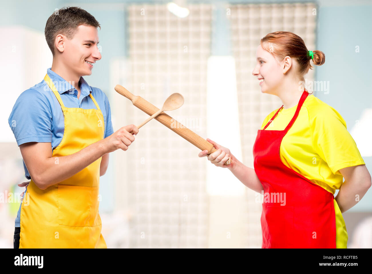 Ritratto di un uomo e di una donna in un grembiule con utensili da cucina di combattimenti in cucina Foto Stock