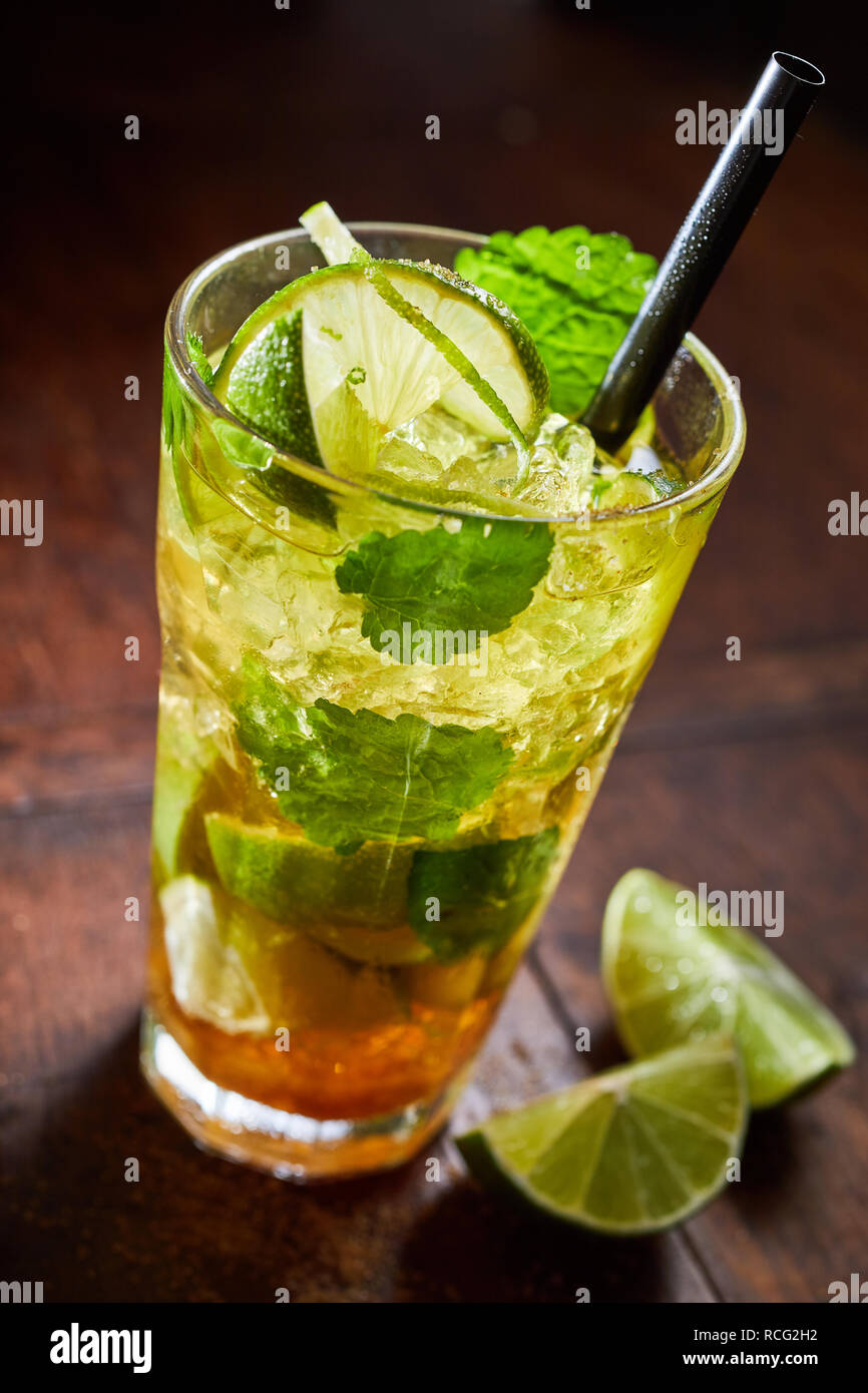 Iced lime cocktail con foglie di menta fresca servita con ghiaccio tritato e una cannuccia in un bicchiere alto su un contatore di legno in un pub o discoteca Foto Stock