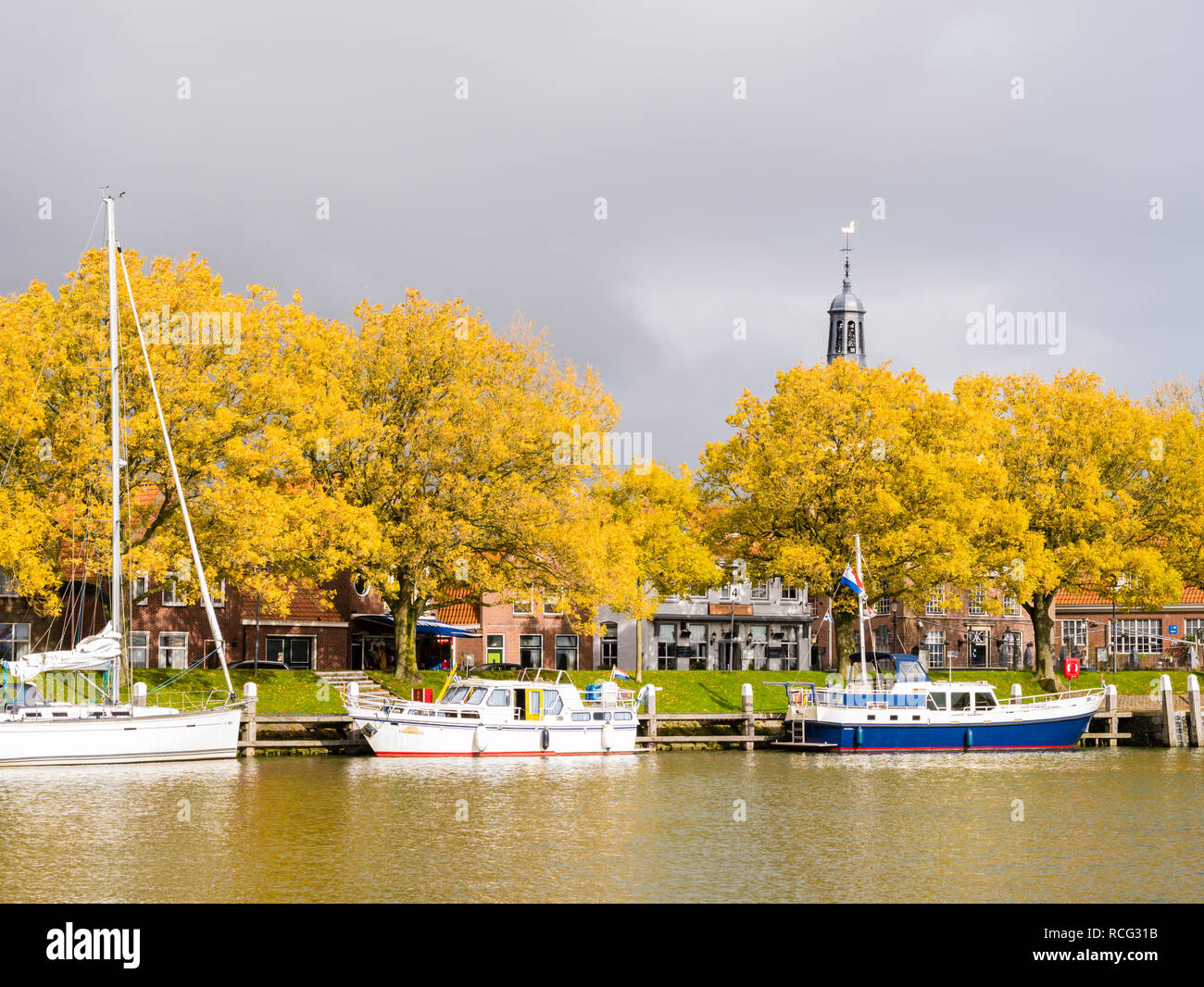 Barche a vela ormeggiata al pontile a marina, gli alberi in autunno colori e nuvole di tempesta, Enkhuizen, Noord-Holland, Paesi Bassi Foto Stock