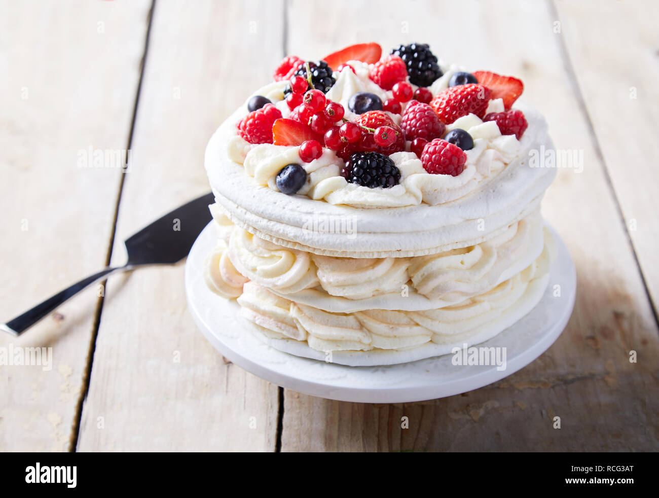 Gourmet torta pavlova con fresco berry topping e strati di panna montata e meringa servita su una piastra con una spatola in una vista ravvicinata Foto Stock