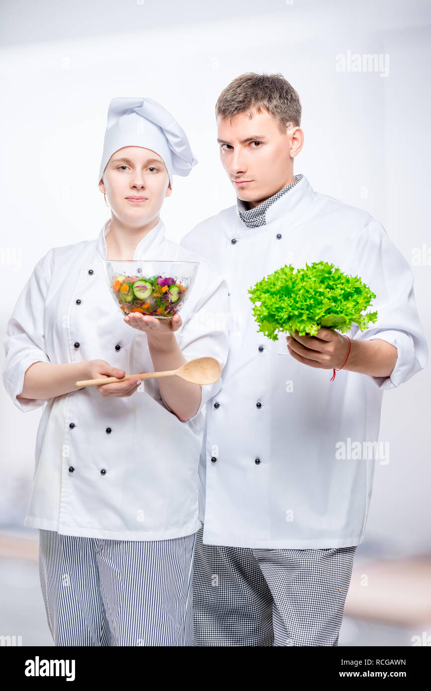 Giovani cuochi in giacca con insalata in mani su sfondo grigio Foto Stock