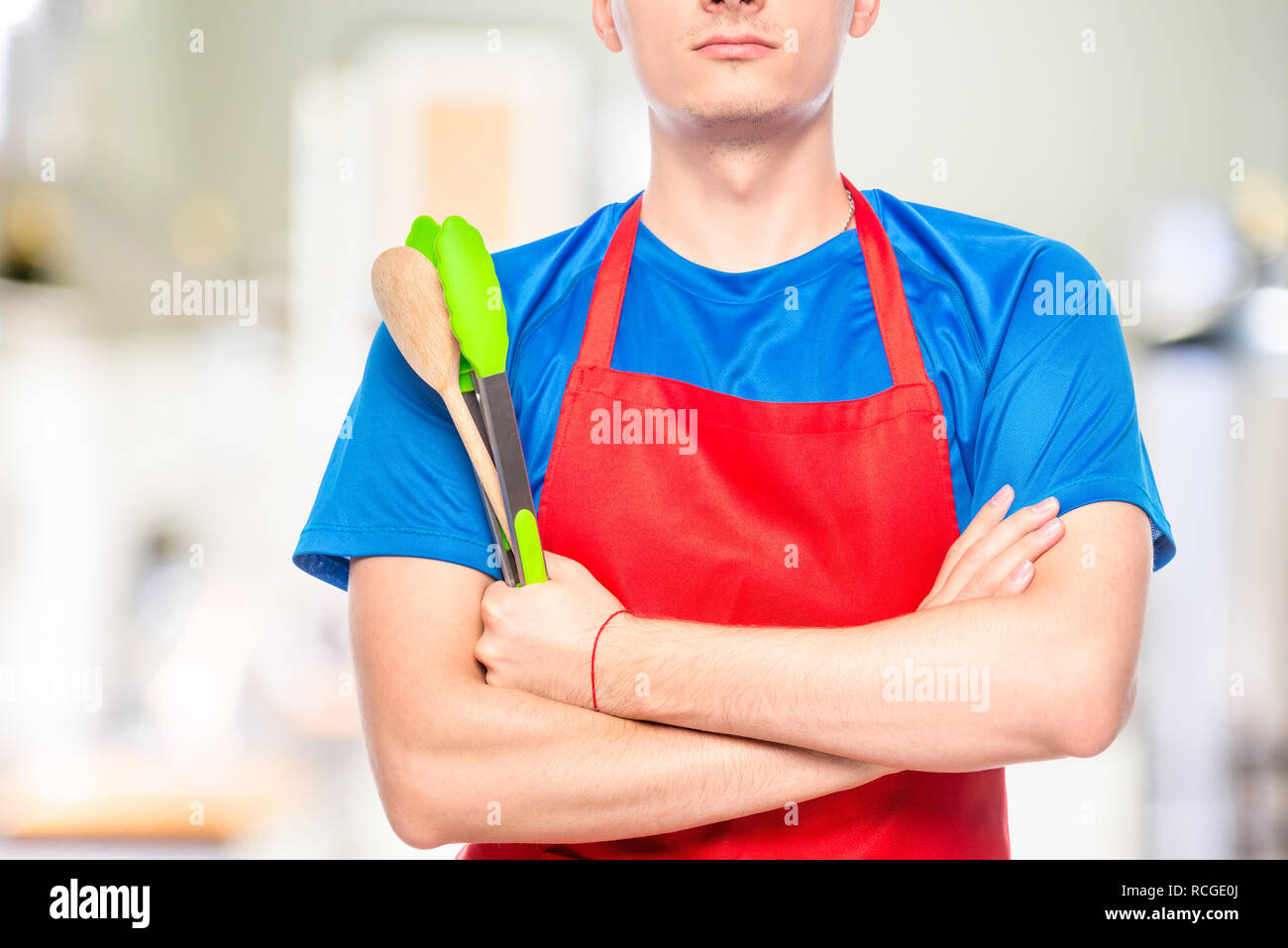 Primo piano di uomo di petto in grembiule con utensili da cucina Foto Stock