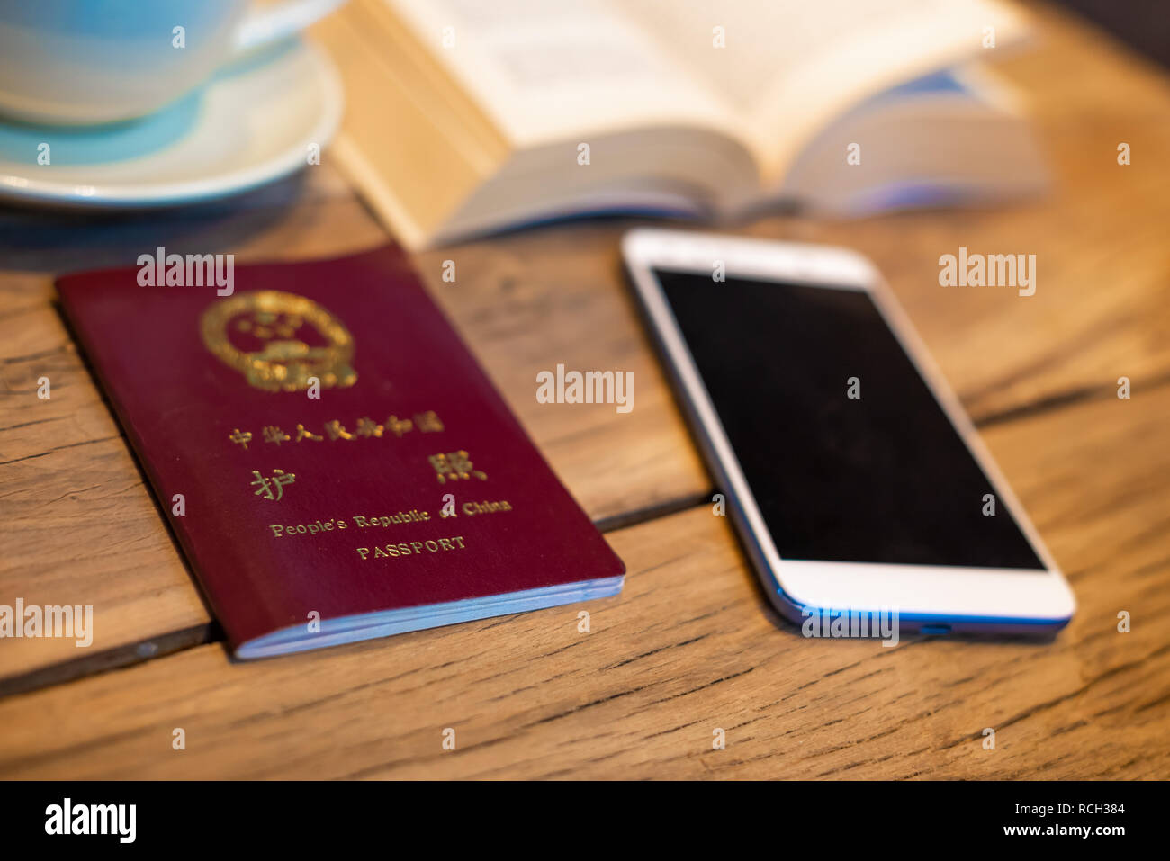 Passaporto cinese e lo smartphone su un tavolo di legno con un libro aperto e la tazza di caffè nella caffetteria Foto Stock