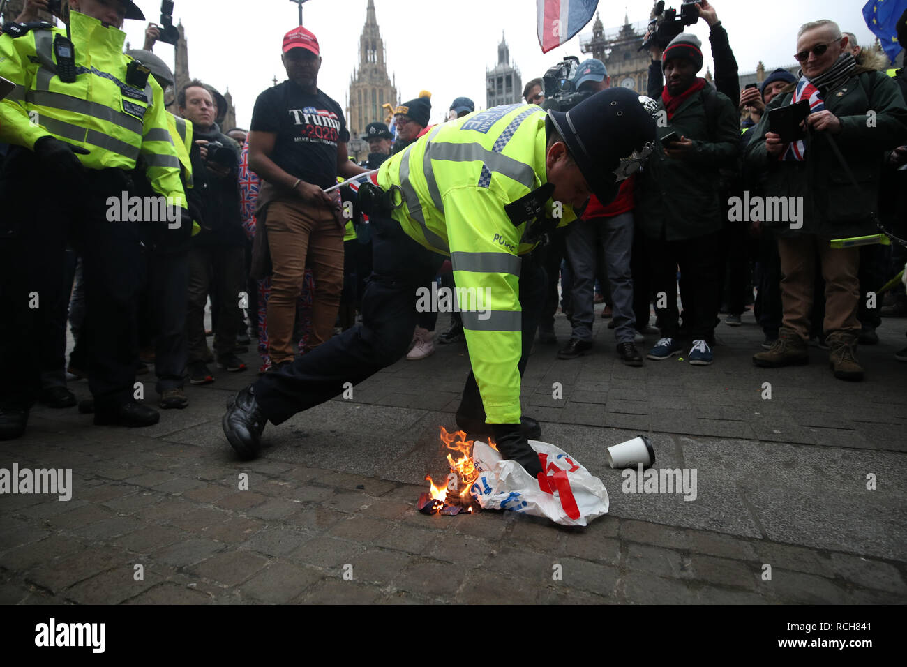 Un funzionario di polizia si estingue una bandiera che è stata flagellata da incendi da pro-Brexit contestatori fuori le case del Parlamento, Londra, davanti alla House of Commons votazione sul primo ministro Brexit della trattativa. Foto Stock