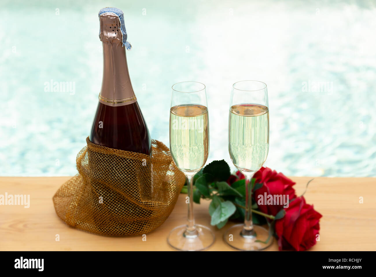 Bottiglia di champagne e bicchieri con rose fiore accanto alla piscina. Foto Stock