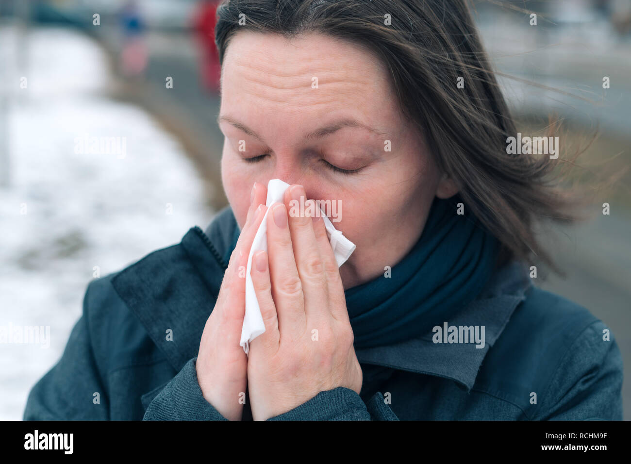 Donna soffia il naso in un fazzoletto di carta per strada in una fredda giornata invernale all'inizio della stagione influenzale Foto Stock