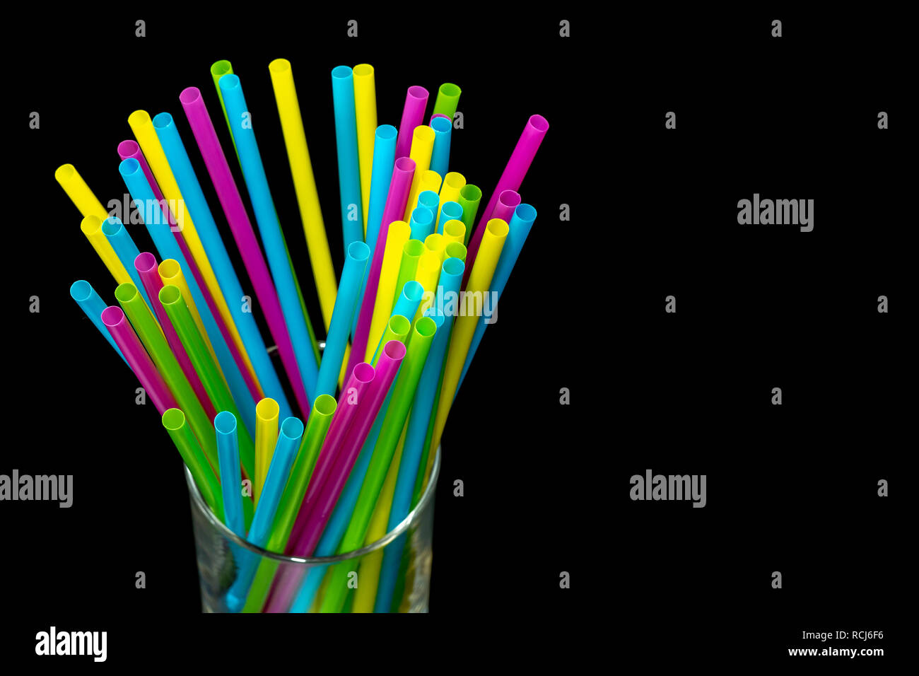 Diversi di plastica colorata cannucce potabile collocato in un bicchiere su sfondo nero.jpg Foto Stock